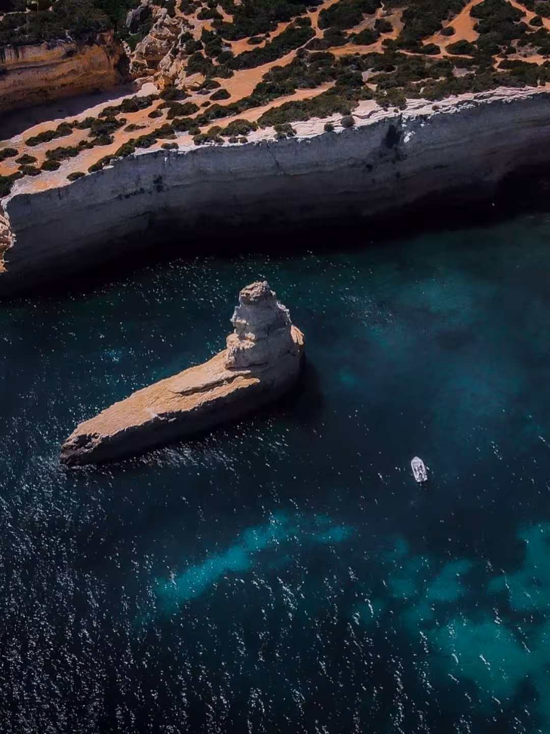 Aerial view of Benagil Cave coastline with turquoise Atlantic water, dramatic limestone cliffs and tour boat exploring Algarve