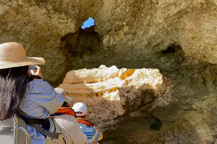 Traveler photographing Algarve sea cave rock formations from a boat on a Benagil caves and coastline cruise