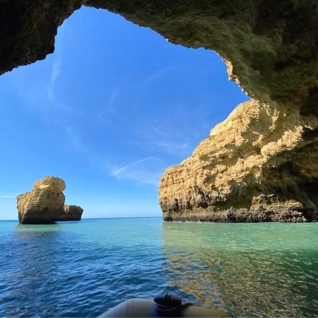 Boat entering turquoise waters beneath towering Algarve cliffs near Benagil cave on scenic Benagil & Dolphins tour