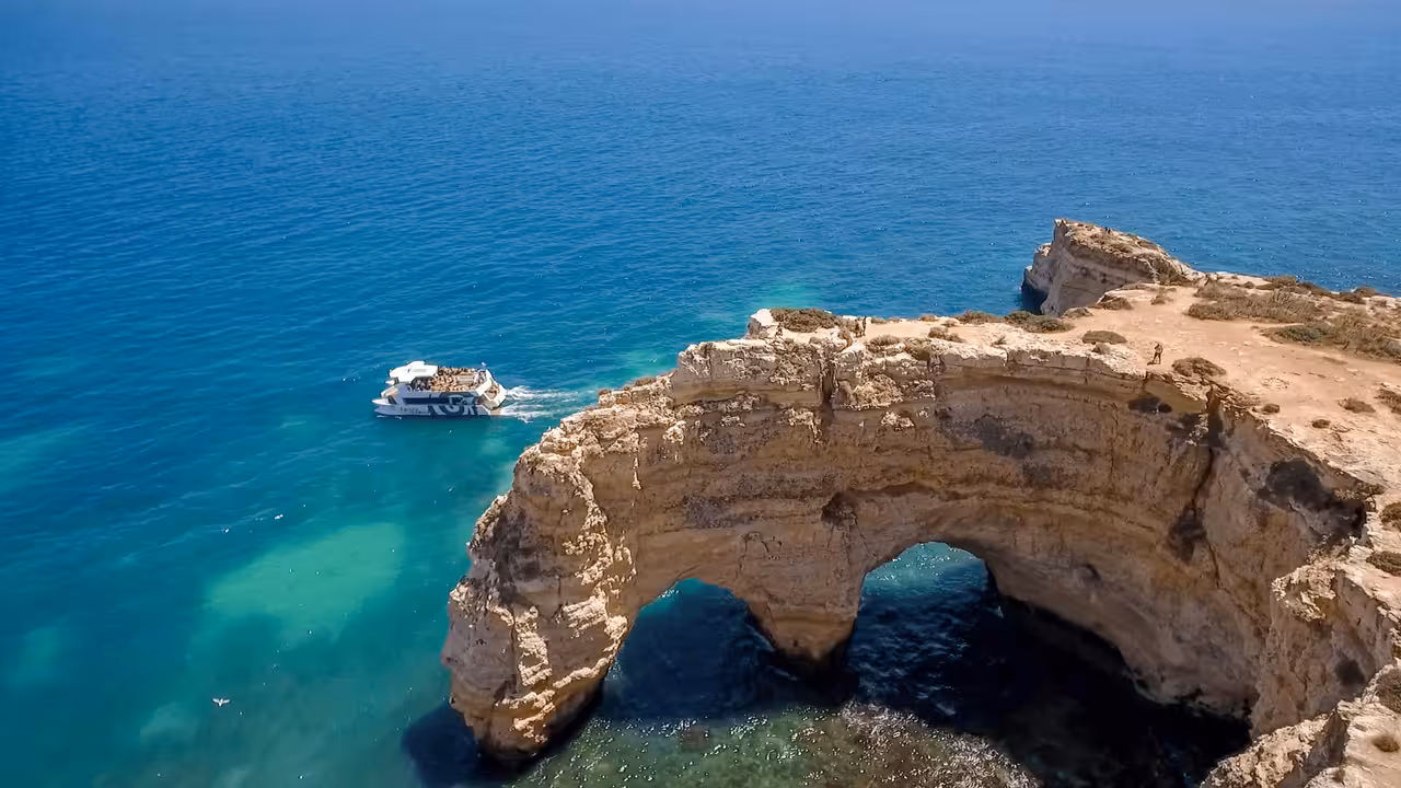 Aerial view of a tour boat cruising past stunning golden limestone cliffs and sea arches on the Albufeira Benagil Caves boat tour