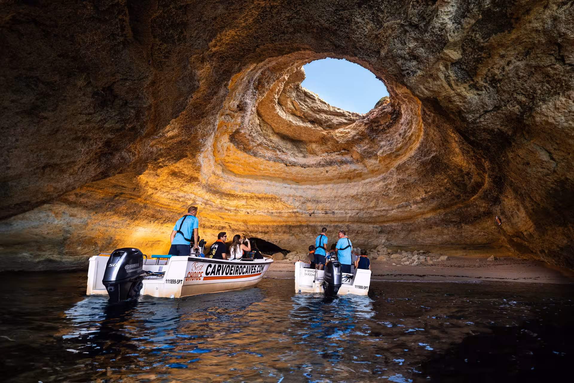 Tourists on a boat tour inside Benagil Cave, admiring the sunlight through the iconic skylight in Algarve, Portugal.