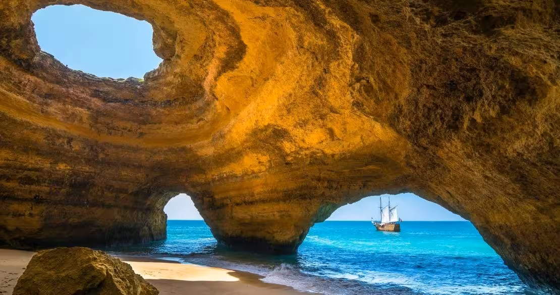 Stunning interior view of Benagil Cave in Algarve with golden limestone arches and a sailing boat on turquoise sea
