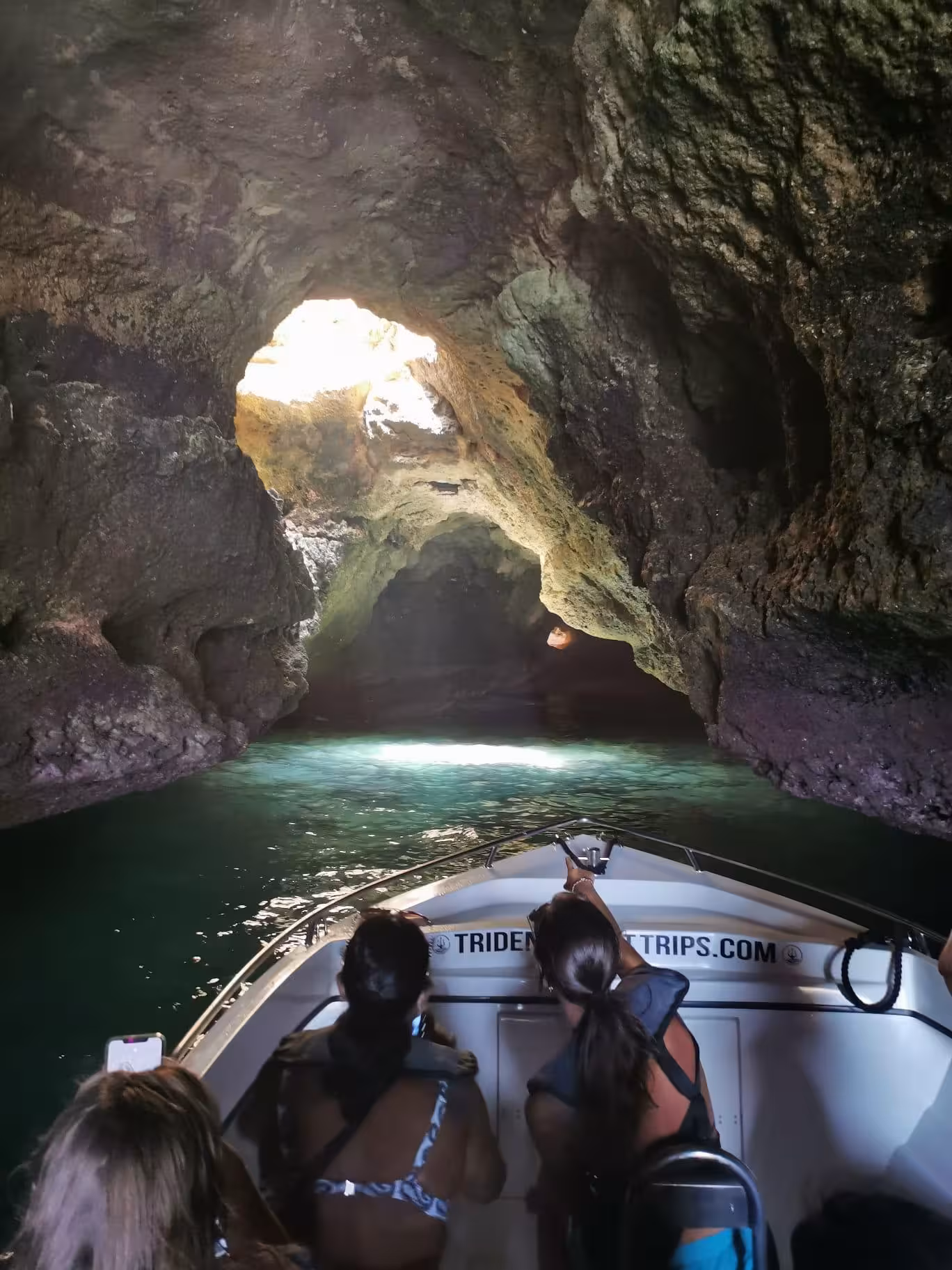Tourists on a boat exploring the glowing emerald waters inside Benagil Cave tunnel during an essential Algarve cave tour