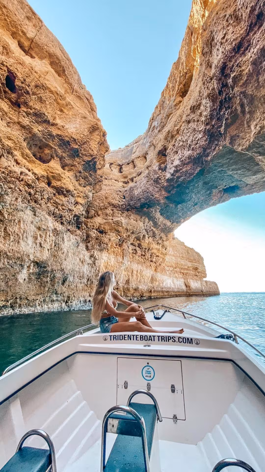 Woman relaxing on a boat bow admiring stunning golden limestone cliffs on an essential Benagil Cave boat tour in Algarve Portugal