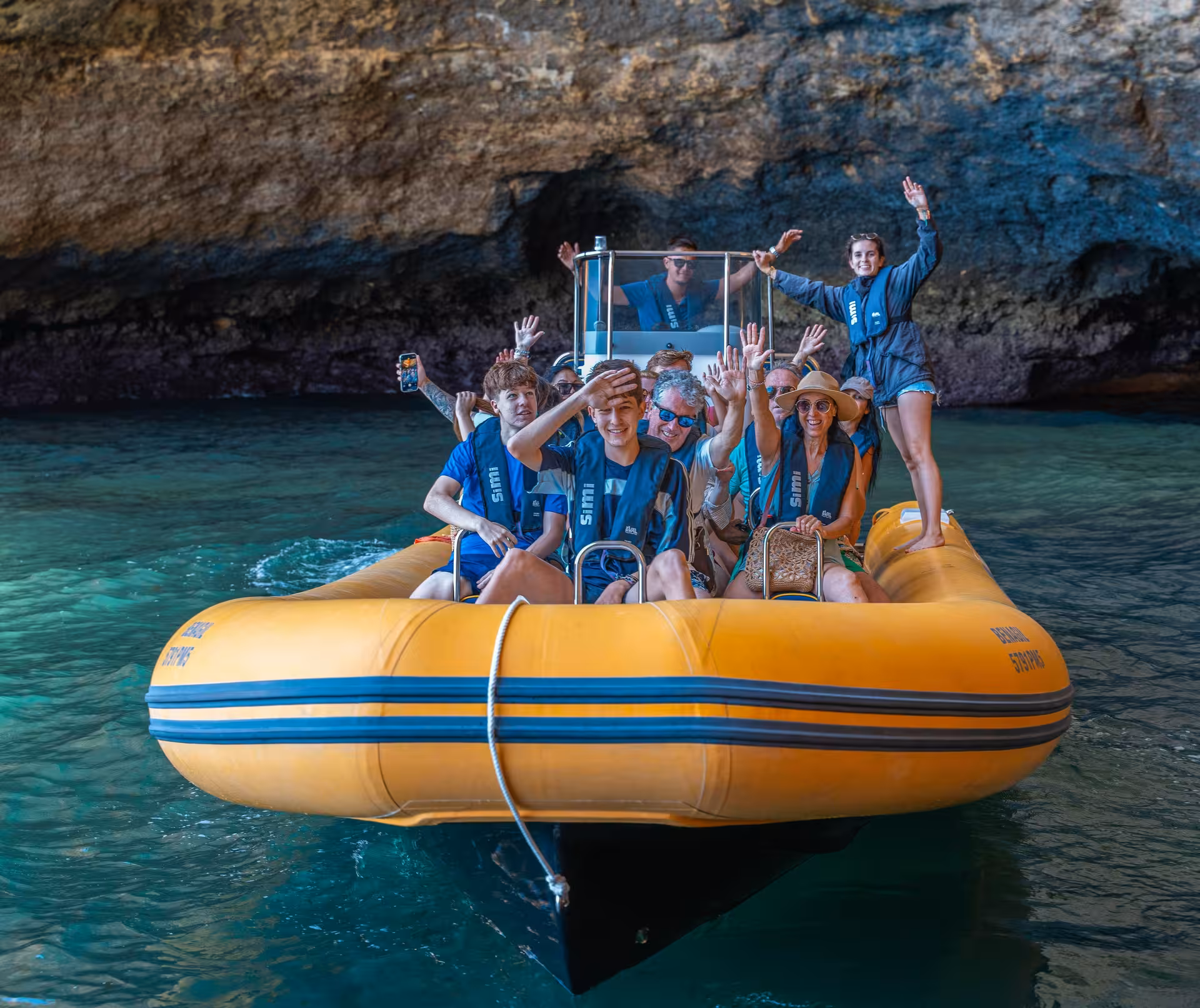 Happy group waving inside Benagil sea cave on a yellow RIB boat tour exploring Algarve's iconic coastal caves Portugal
