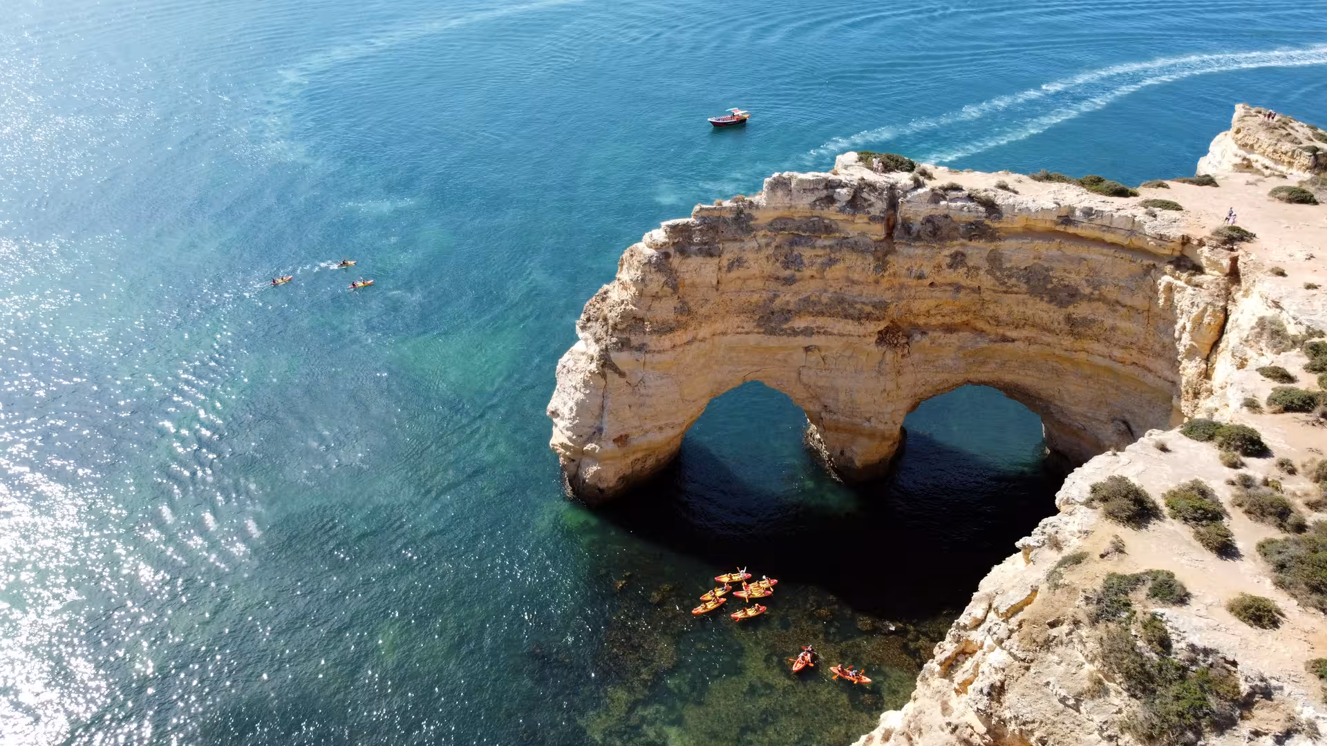 Aerial view of Benagil sea cave rock arches with kayakers and a tour boat on turquoise Algarve waters