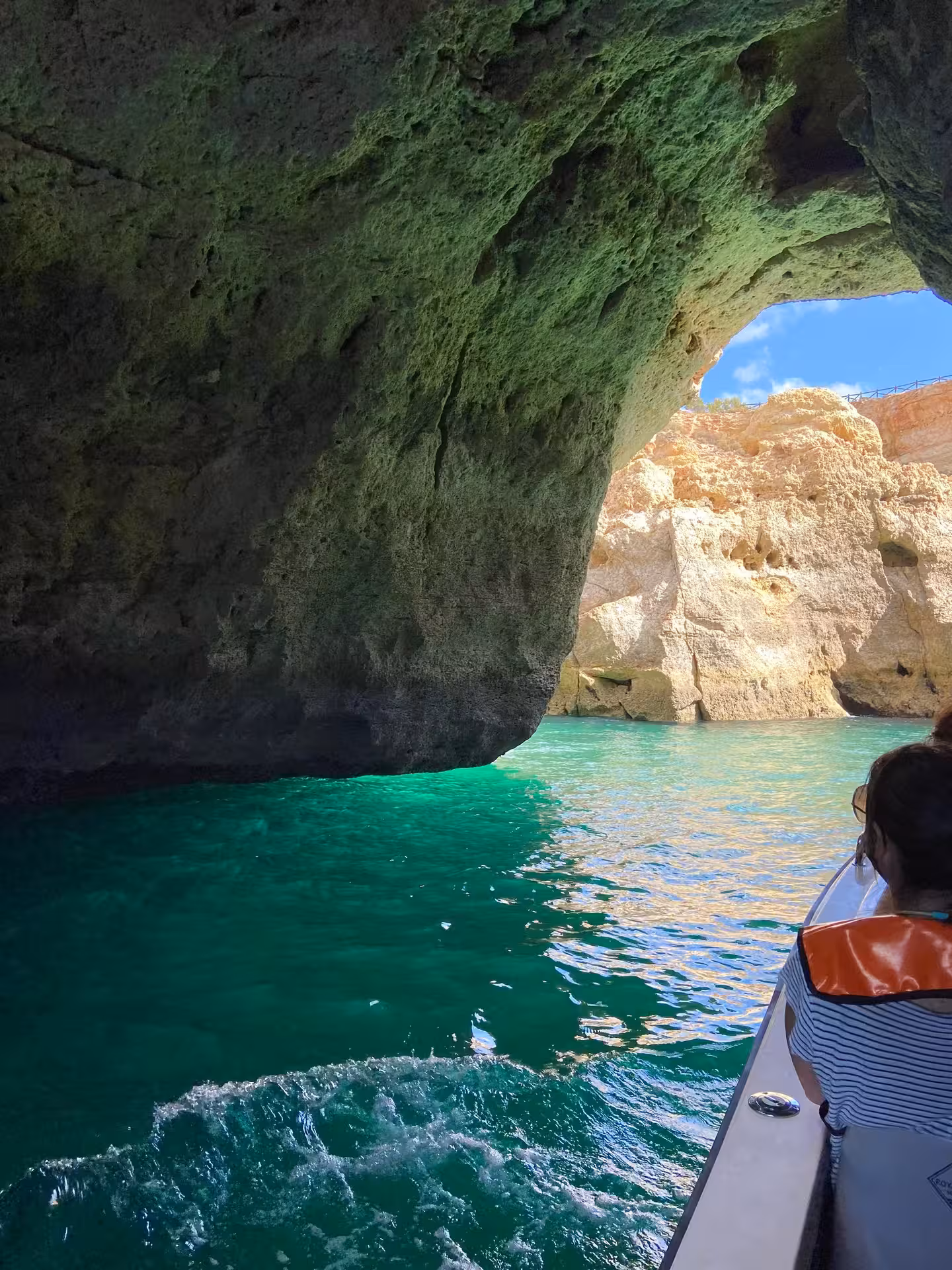 Small boat gliding through emerald water inside Benagil Cave, revealing towering Algarve cliffs and sunlit rock ceiling