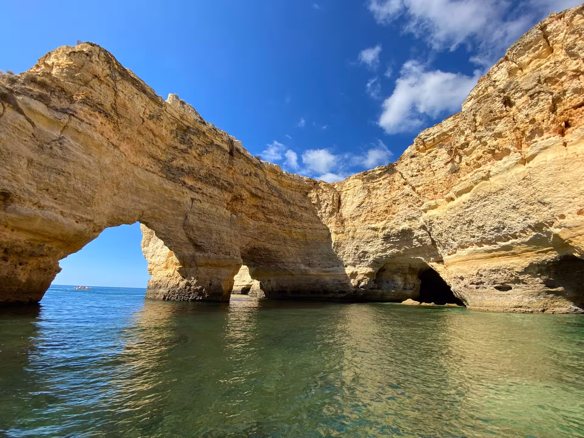 Boat tour view of Benagil Cave’s golden limestone arch and turquoise Algarve sea on a sunny Portugal coast day