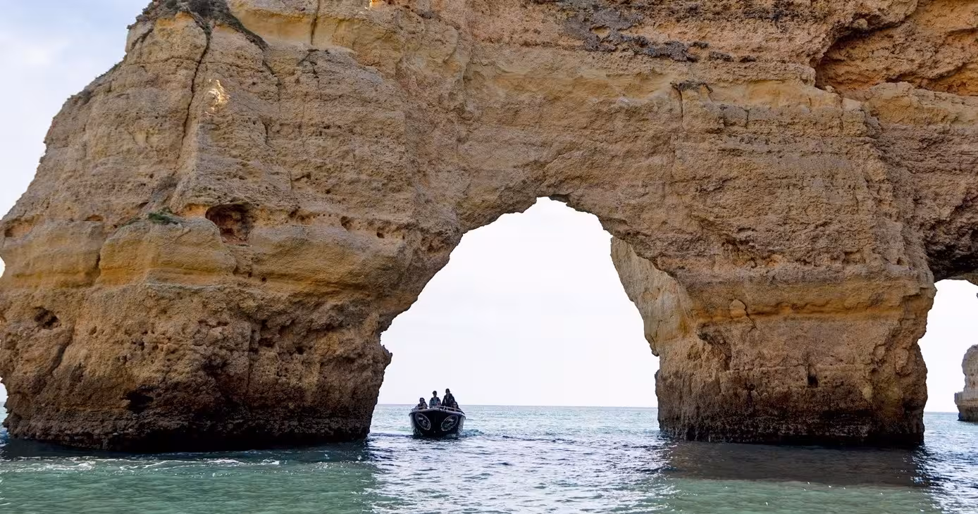 Small tour boat cruising through dramatic sea arch rock formation on the Classic Private Benagil 1H cave and coastline trip