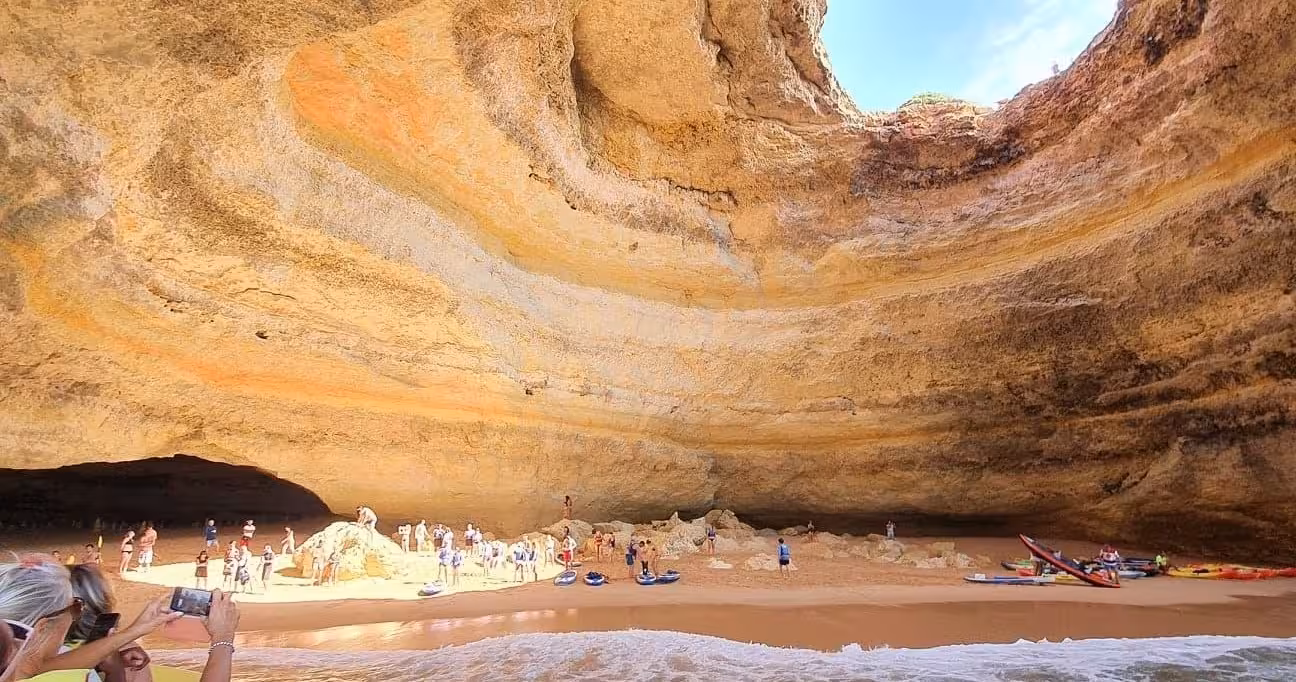 People explore the sunlit interior of Benagil Cave, surrounded by its iconic orange and yellow rock formations in Algarve.