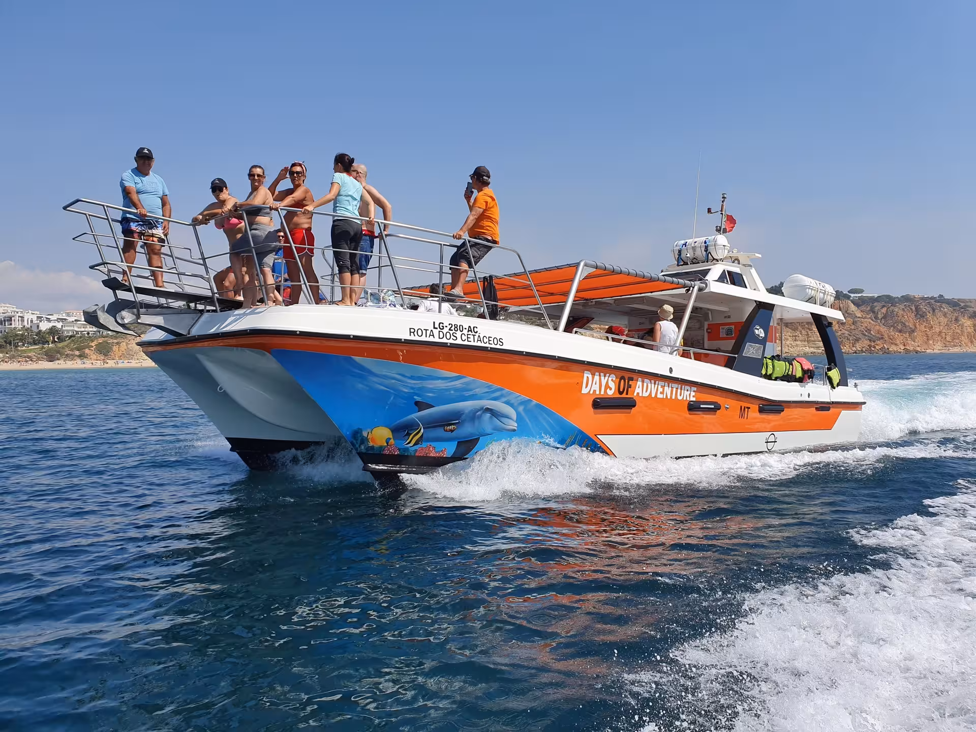 Days of Adventure catamaran with tourists on deck cruising along the Algarve coast from Lagos to Benagil Cave