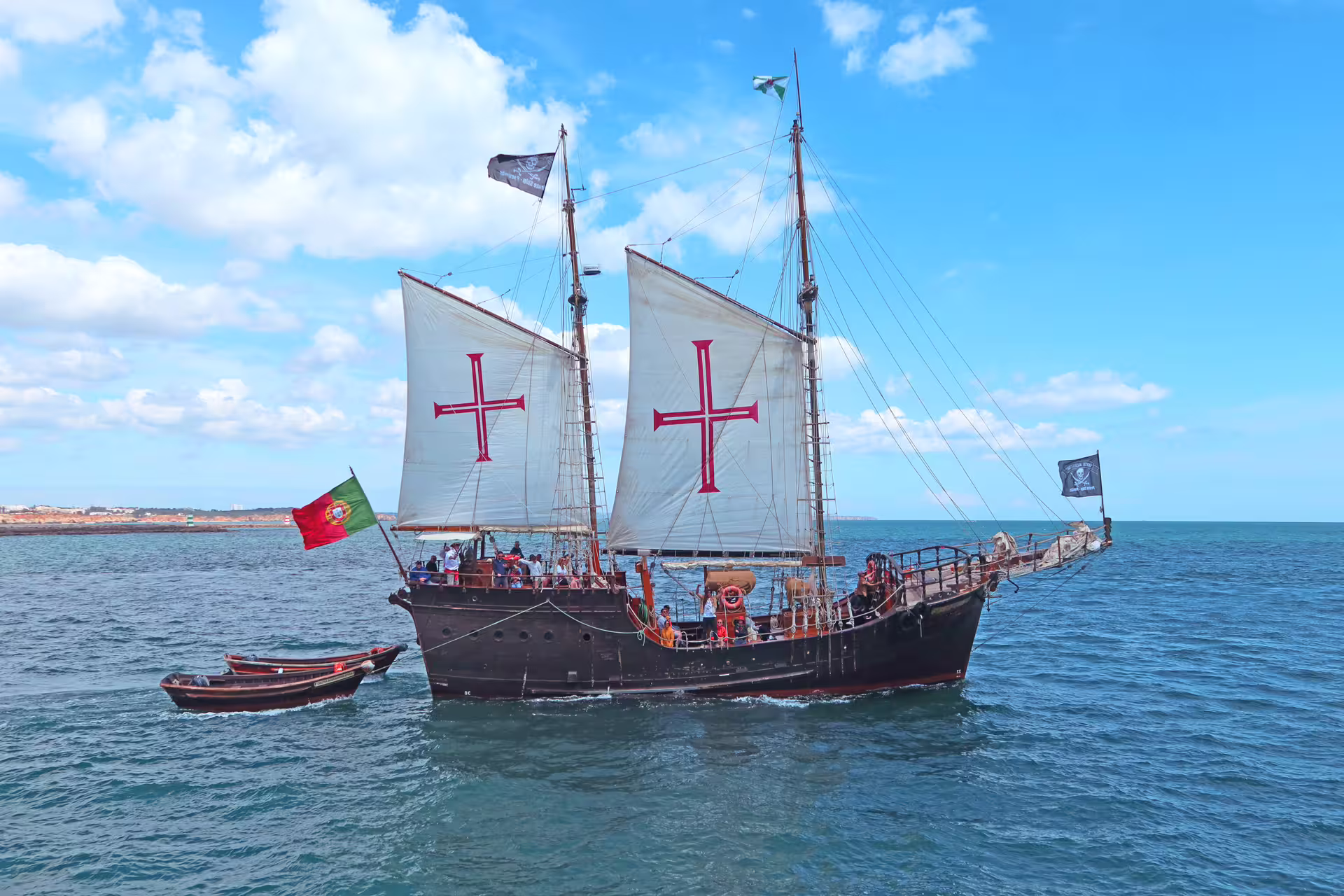 Sailing ship with Portuguese flag on a sunny day during the Benagil cave cruise, showcasing stunning Algarve coast views.