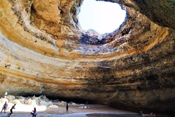 Visitors exploring the sunlit Benagil sea cave and sandy beach on the Benagil & Dolphins Tour in the Algarve, Portugal