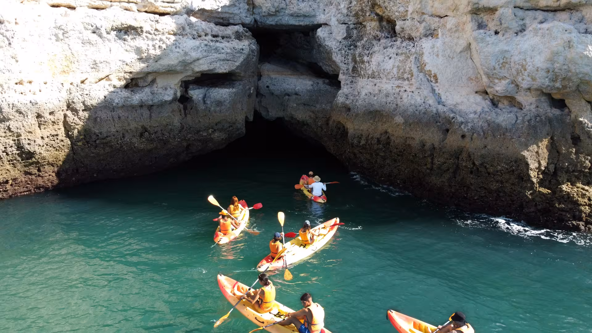 Kayakers in life vests paddling toward a scenic Algarve sea cave on a Benagil boat tour from Portimao