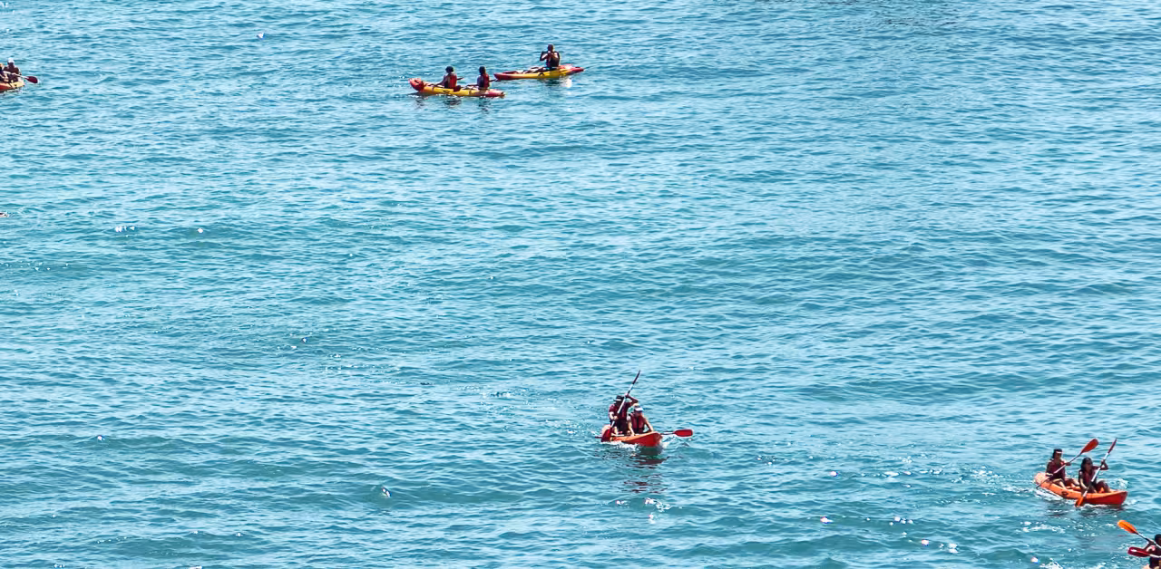 Small groups paddle bright kayaks across calm turquoise Atlantic waters on a Benagil Cave guided kayak express tour