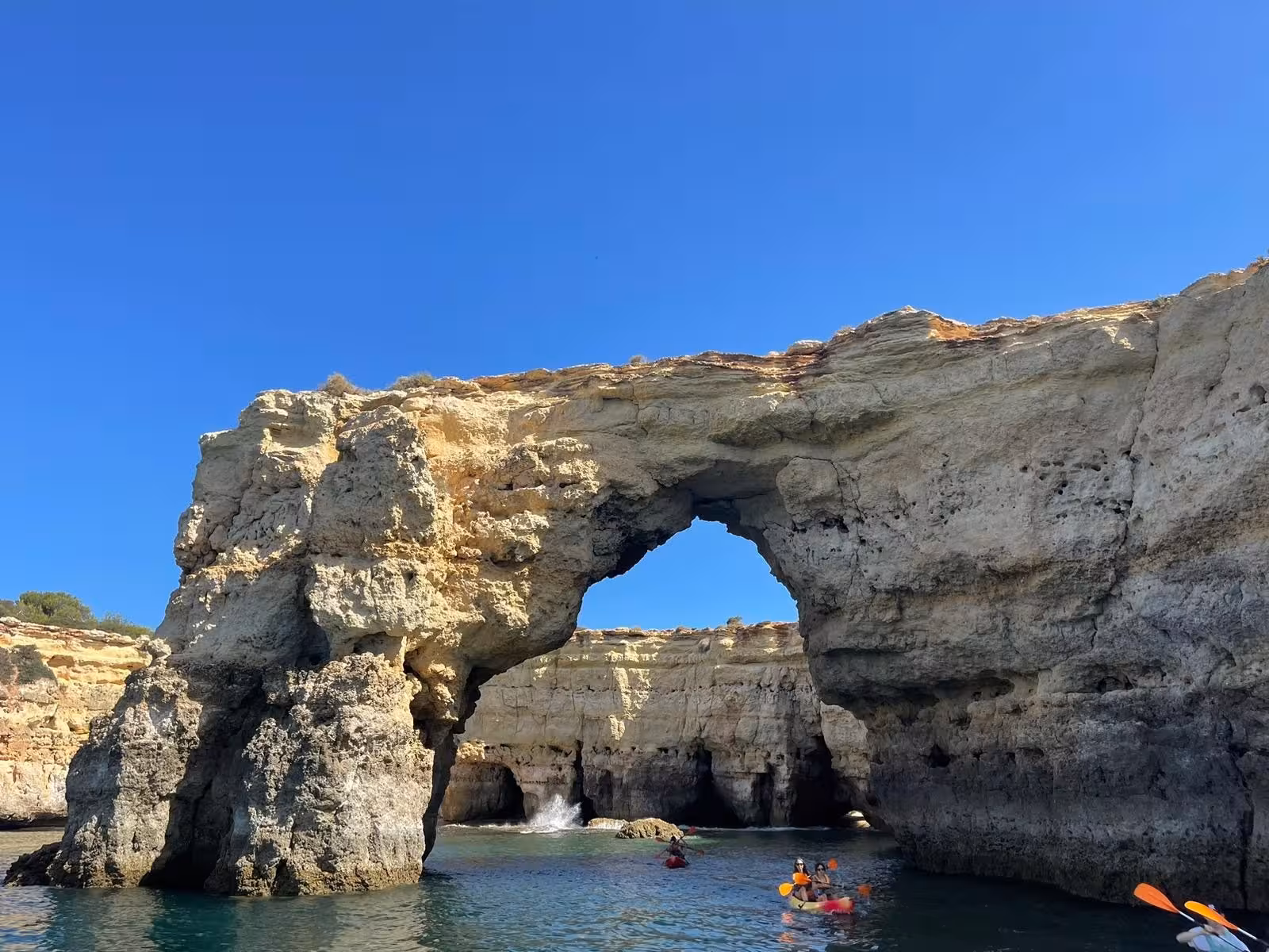 Kayakers paddle beneath dramatic limestone arch near Benagil Cave on Algarve coast during guided dolphin and grotto tour