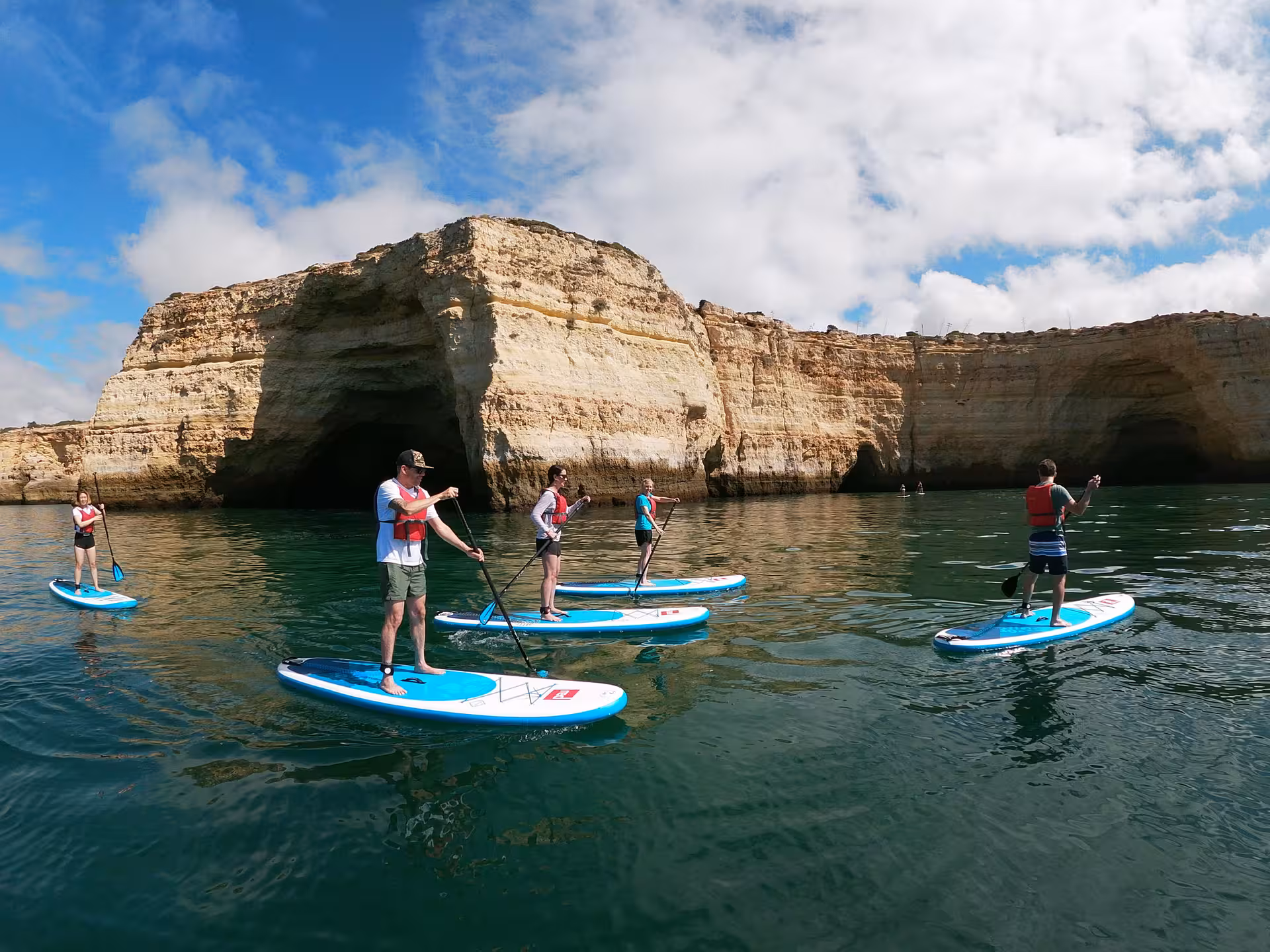 Group paddleboarding near Benagil Cave cliffs in Algarve, Portugal, exploring sea caves on a guided SUP adventure tour