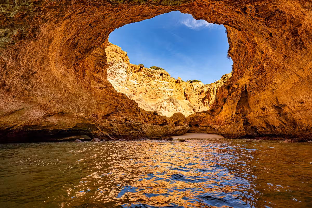 Stunning view of the Benagil Cave with sunlight illuminating the golden rock formations and azure waters.