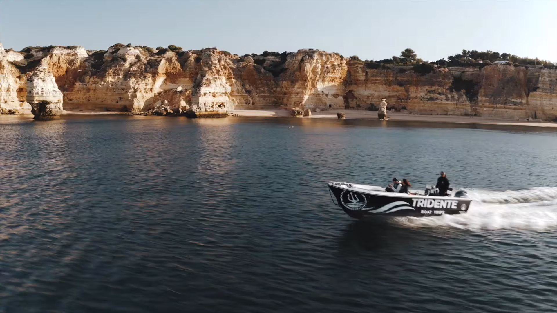 Tridente private speedboat cruising along the golden limestone cliffs of Algarve coastline on an exclusive Benagil Cave deluxe boat tour in Portugal.