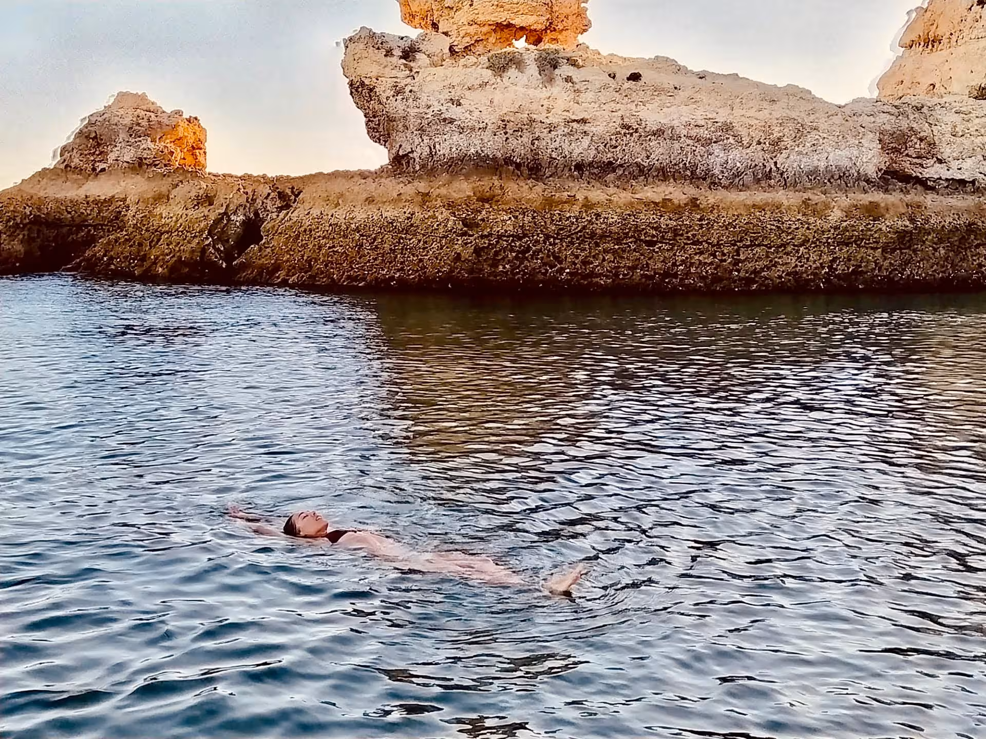 Solo traveler enjoys peaceful swim near rocky Algarve coastline on serene private tour experience.