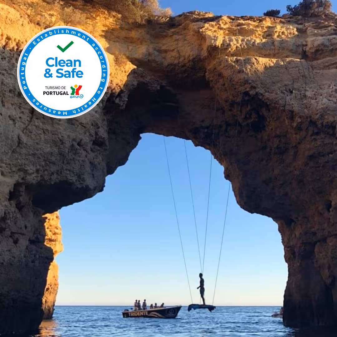 Silhouette of a person suspended by ropes over the sea framed by stunning Benagil Cave rock arch on a private deluxe boat tour in Algarve Portugal.