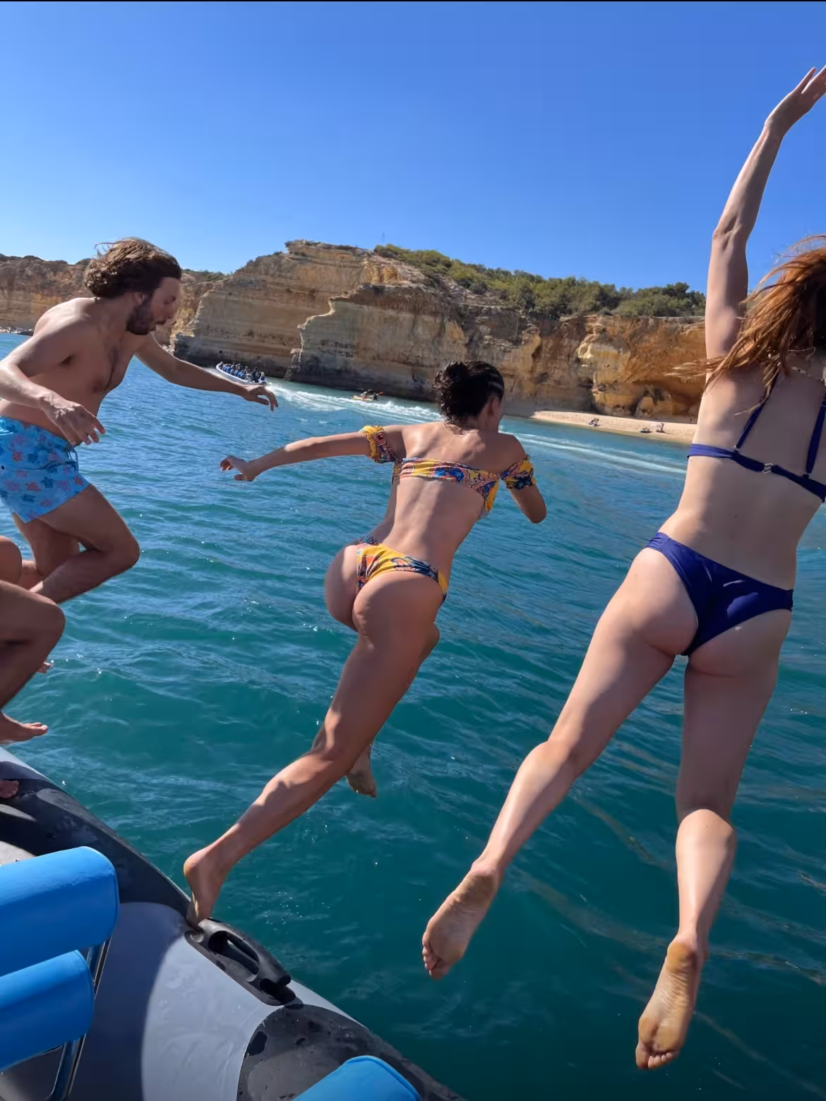Adventurous group jumps off boat into clear Algarve waters during private tour, showcasing exciting ocean fun.