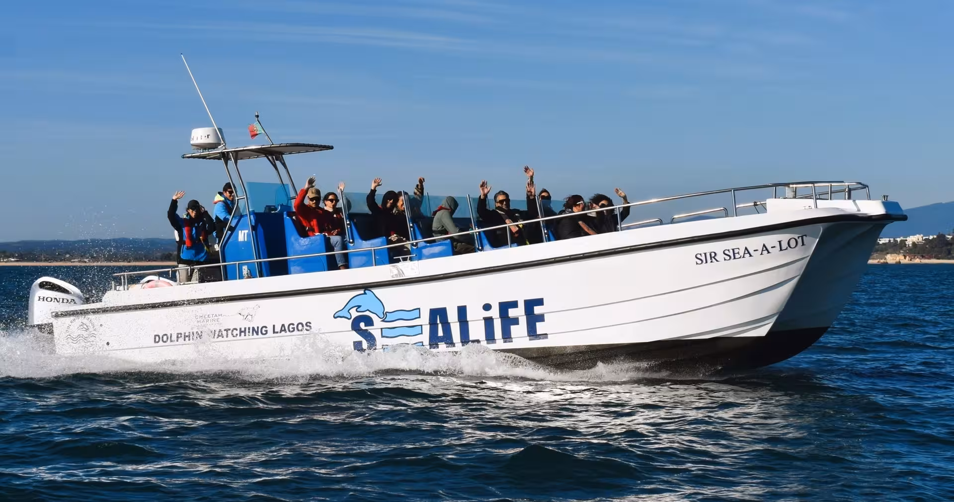 Speedboat with happy passengers on a Benagil cave and dolphin watching tour cruising the Algarve coast near Lagos, Portugal