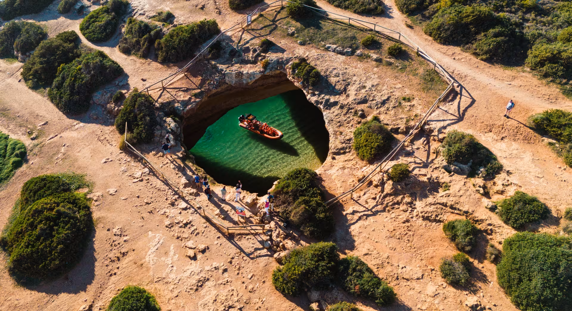 Aerial view of iconic Benagil Cave in Algarve Portugal with orange speed boat inside turquoise lagoon and tourists exploring