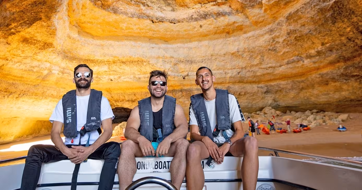 Friends smiling on a speedboat inside Benagil Cave, enjoying a Classic Private Benagil 1H tour with kayakers on the beach