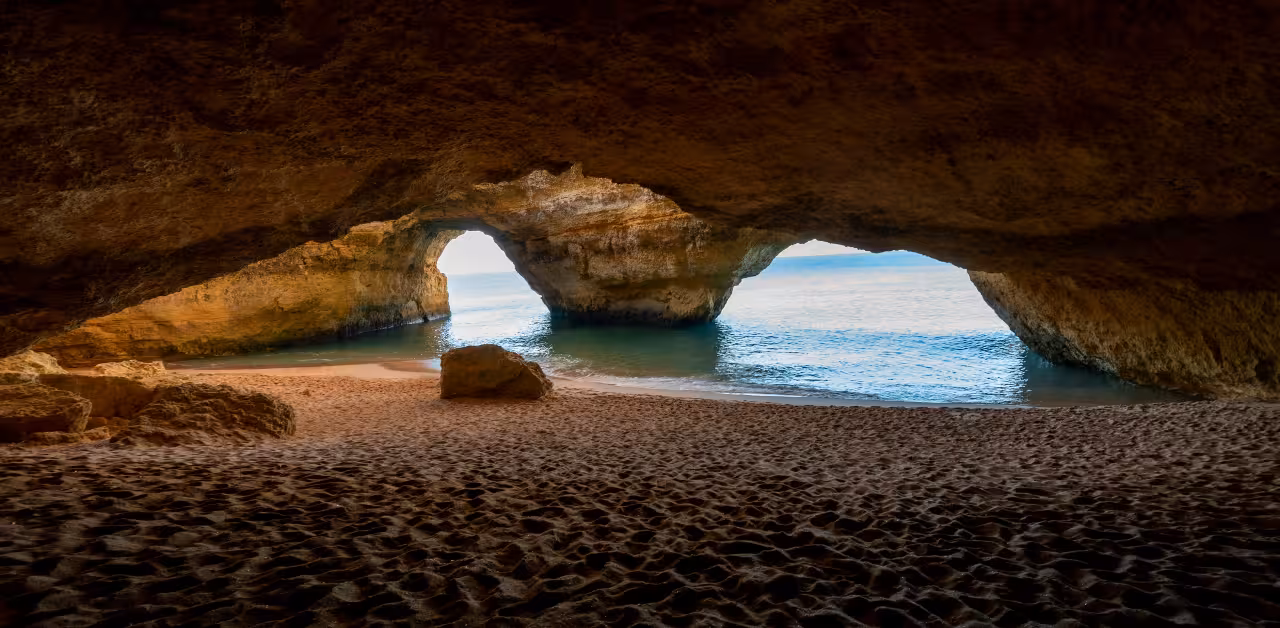 Sunrise view from inside Benagil Cave with golden sand beach, rock arches and calm Atlantic waves on Algarve kayak tour