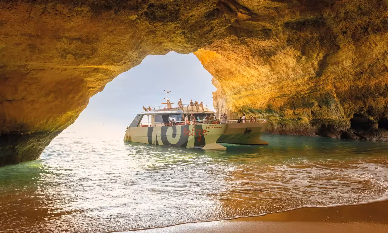 Tour boat seen from inside Benagil Cave golden limestone arch on a scenic Algarve sunset boat tour from Albufeira