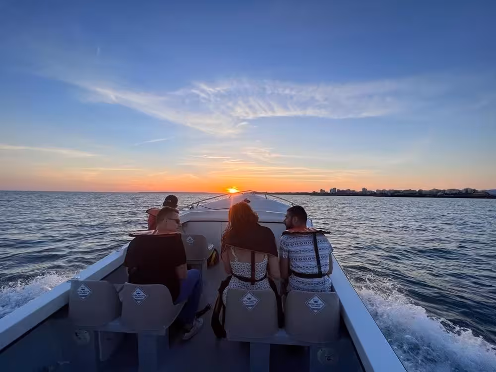 Small group enjoying a Benagil Cave boat tour at sunset, cruising the Algarve coast with golden sky and calm Atlantic waves