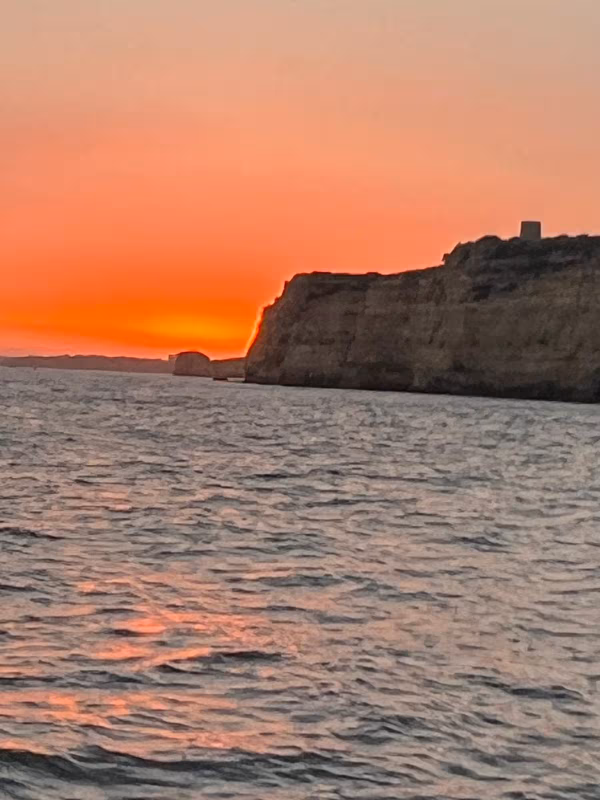 Sunset Benagil Cave boat tour along Algarve cliffs with glowing orange sky reflected on the Atlantic Ocean waves