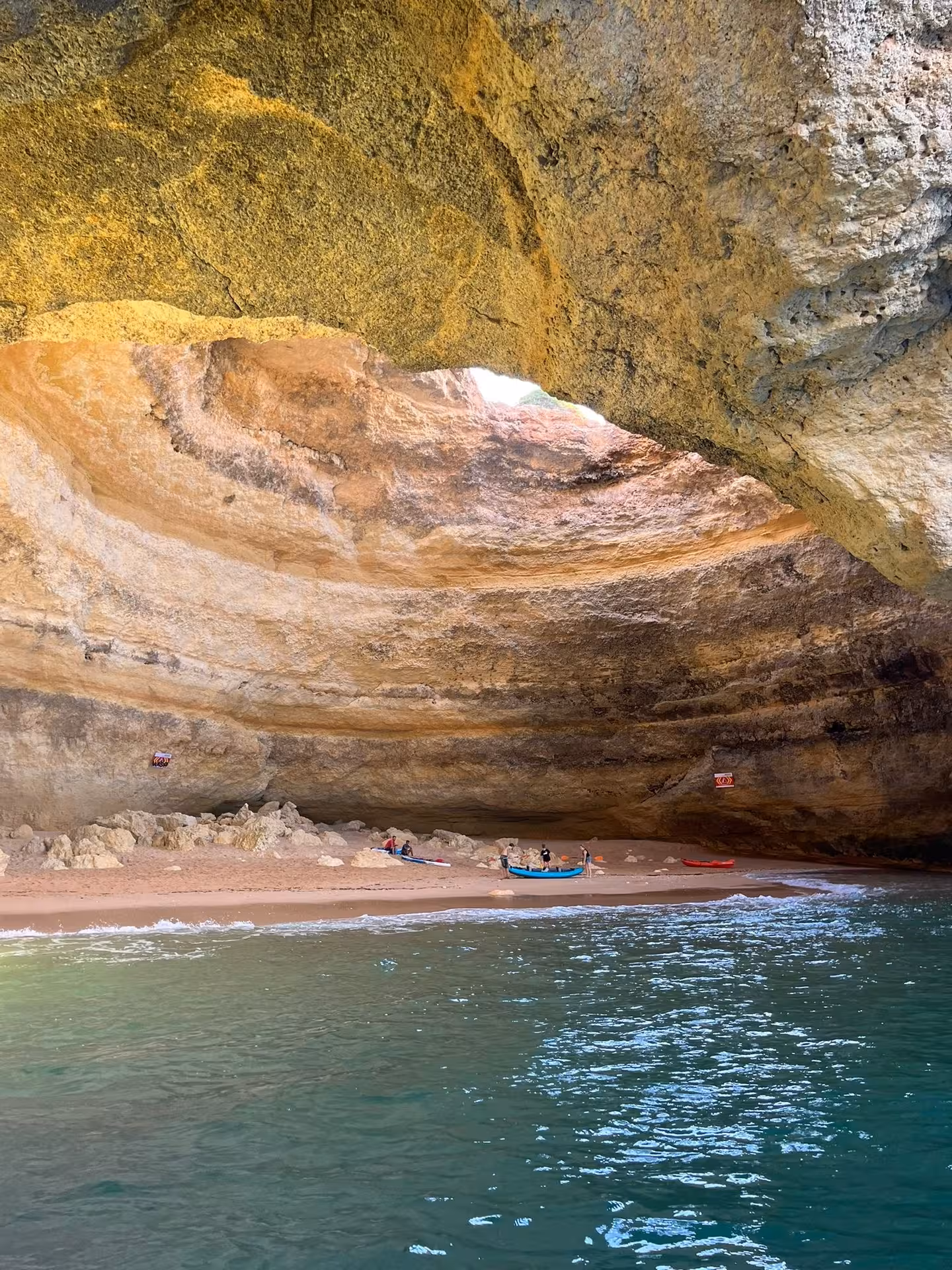Small tour boat and visitors on the hidden beach inside Benagil Cave, Algarve coast, seen from the turquoise sea entrance