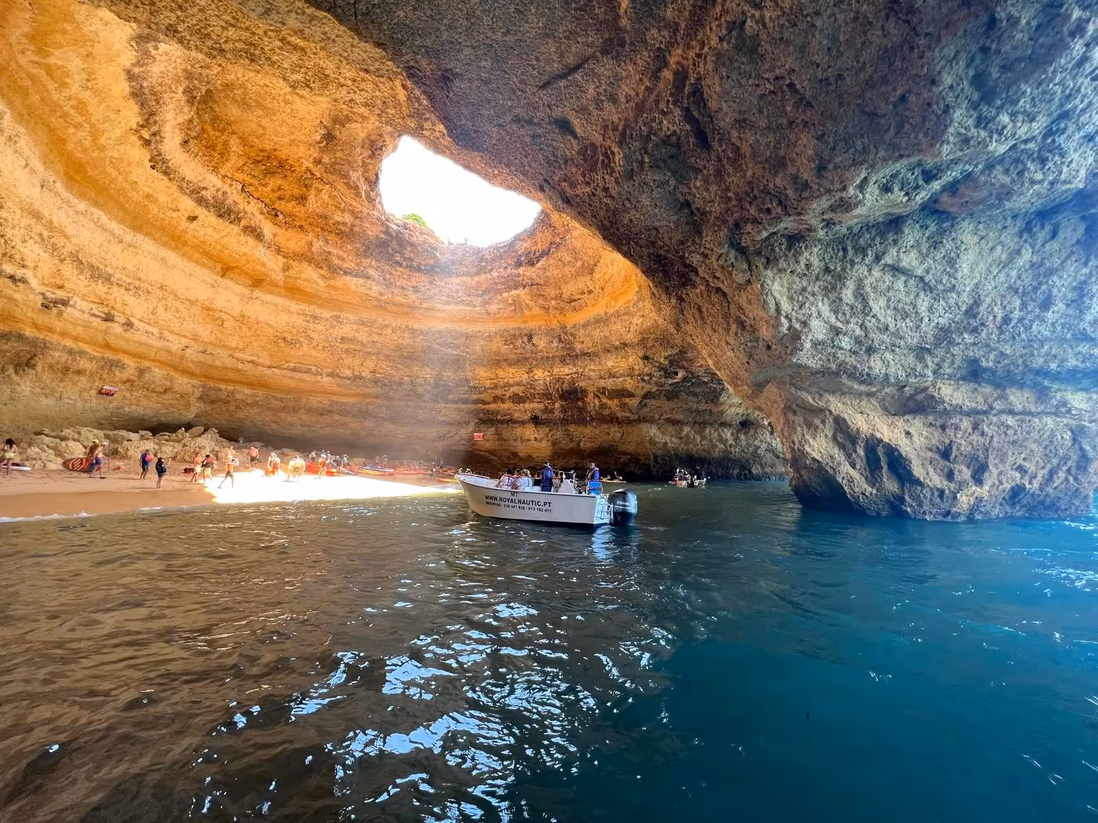 Tour boat enters Benagil Cave in Algarve, Portugal, revealing turquoise water, golden cliffs and sunlit sandy beach inside