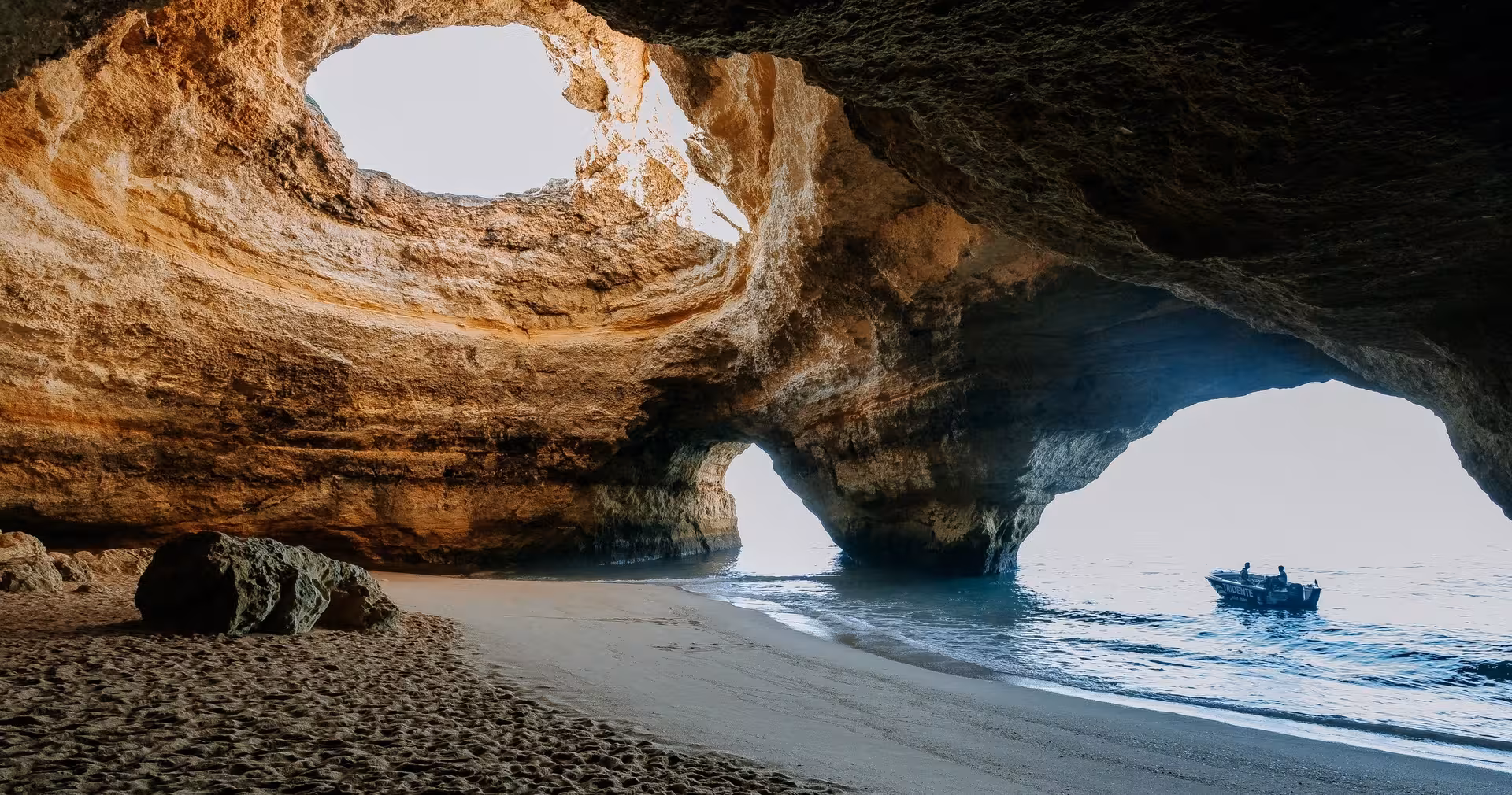 Small tour boat enters Portugal’s famous Benagil Cave, revealing golden rock arches, hidden beach and Atlantic Ocean views