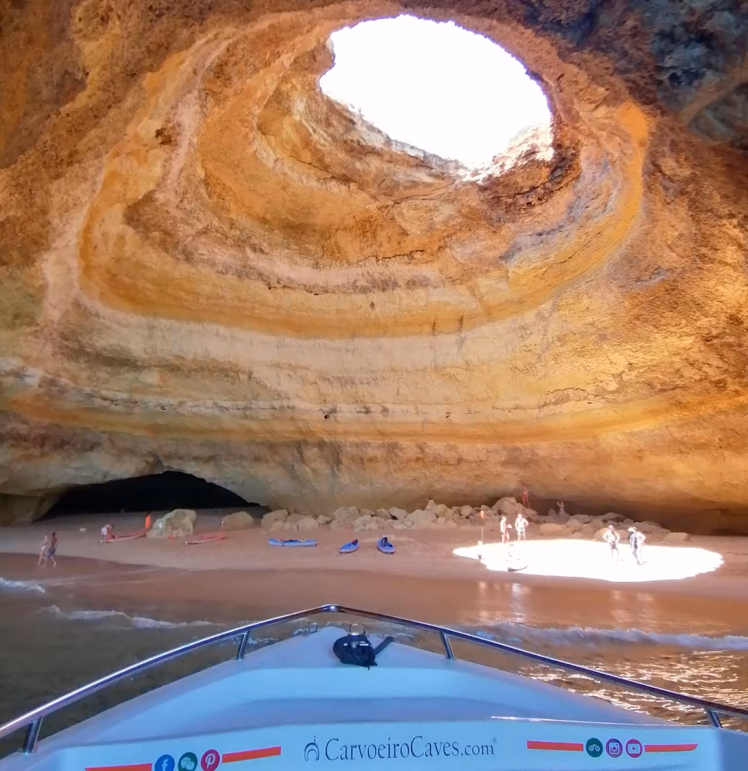 Inside Benagil Cave, a tour boat approaches the sandy shore under the famous skylight opening.