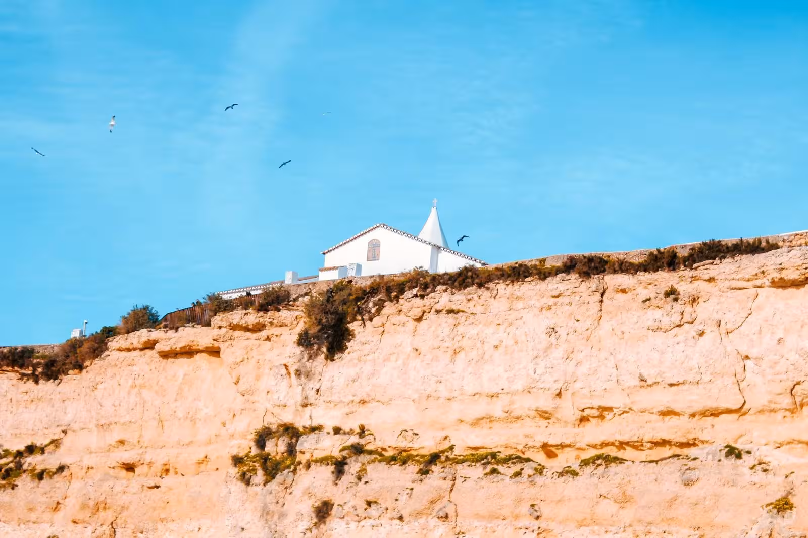 White cliff-top chapel overlooking the Algarve coast, seen from the sea on a private Benagil Cave boat tour, Portugal