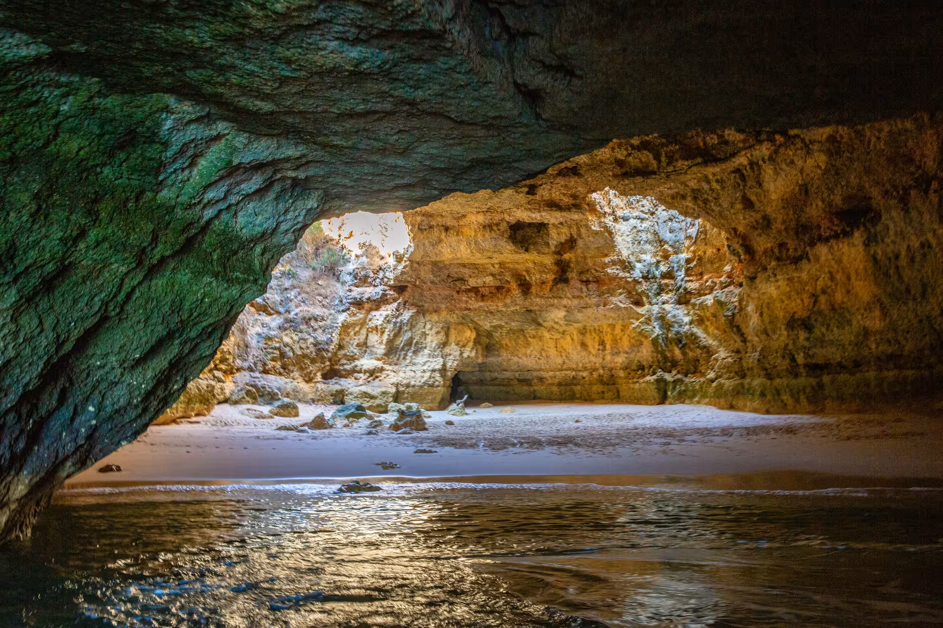 Sunlit sandy beach hidden inside Benagil Cave, seen from the tour boat with golden cliffs and calm Algarve waters