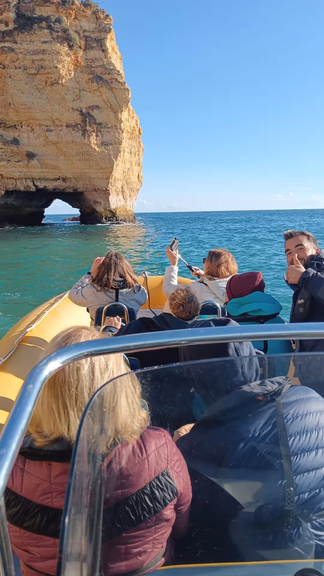 Tourists photographing stunning golden limestone sea arches on a Benagil Caves boat tour along the Algarve coastline Portugal
