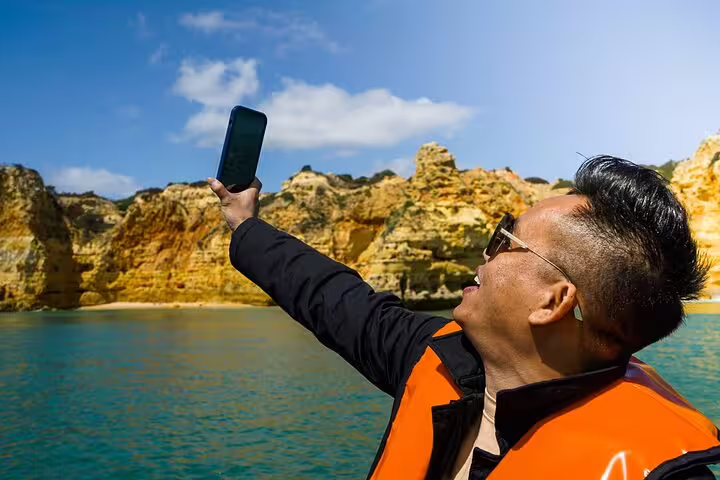 Traveler in a life jacket takes a selfie with stunning cliffs during a boat tour of the Benagil caves on an Algarve day trip.