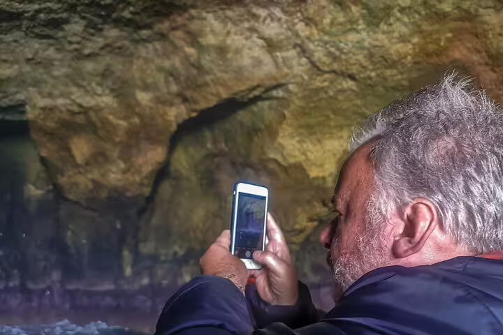 Man capturing the stunning Benagil caves on a smartphone during a boat trip on the Algarve full-day private tour from Lisbon.