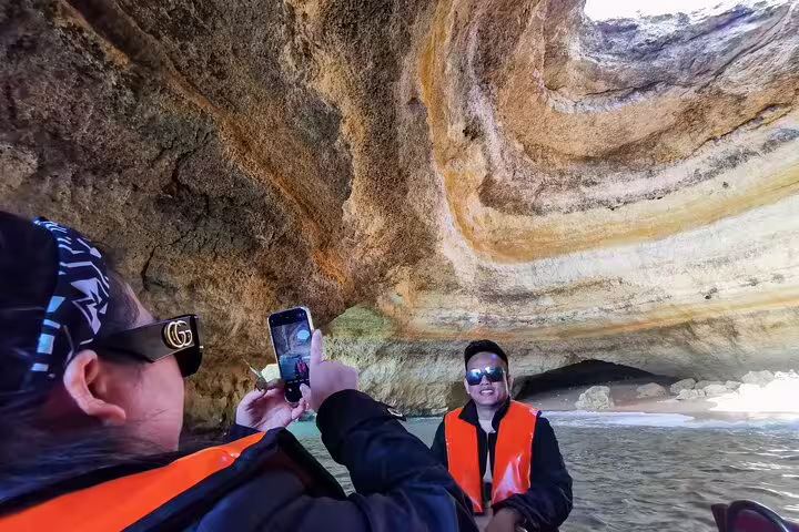 Tourists enjoy a boat trip inside the stunning Benagil Caves during a private Algarve tour from Lisbon, capturing memories.