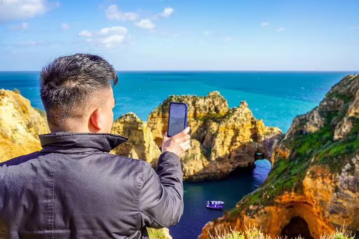Tourist capturing stunning view of Benagil caves and turquoise sea during Comporta to Algarve private tour with boat trip.