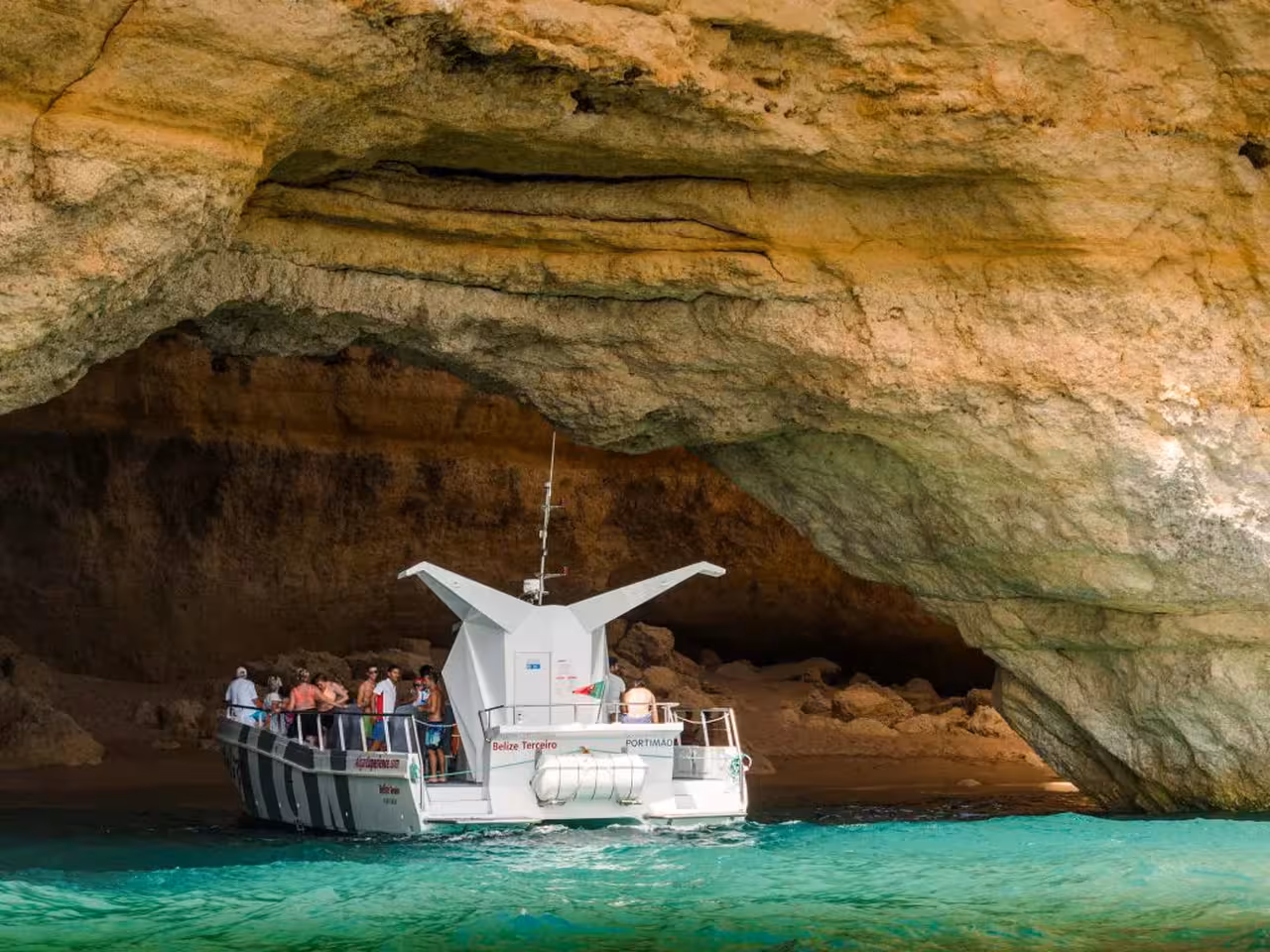 Portimao catamaran tour boat exploring the stunning golden rock arches of Benagil Caves with turquoise waters