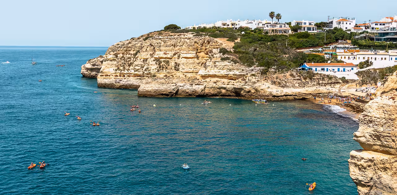 Colorful kayaks paddle along the dramatic Benagil coastline, exploring Algarve sea caves beneath whitewashed cliffs