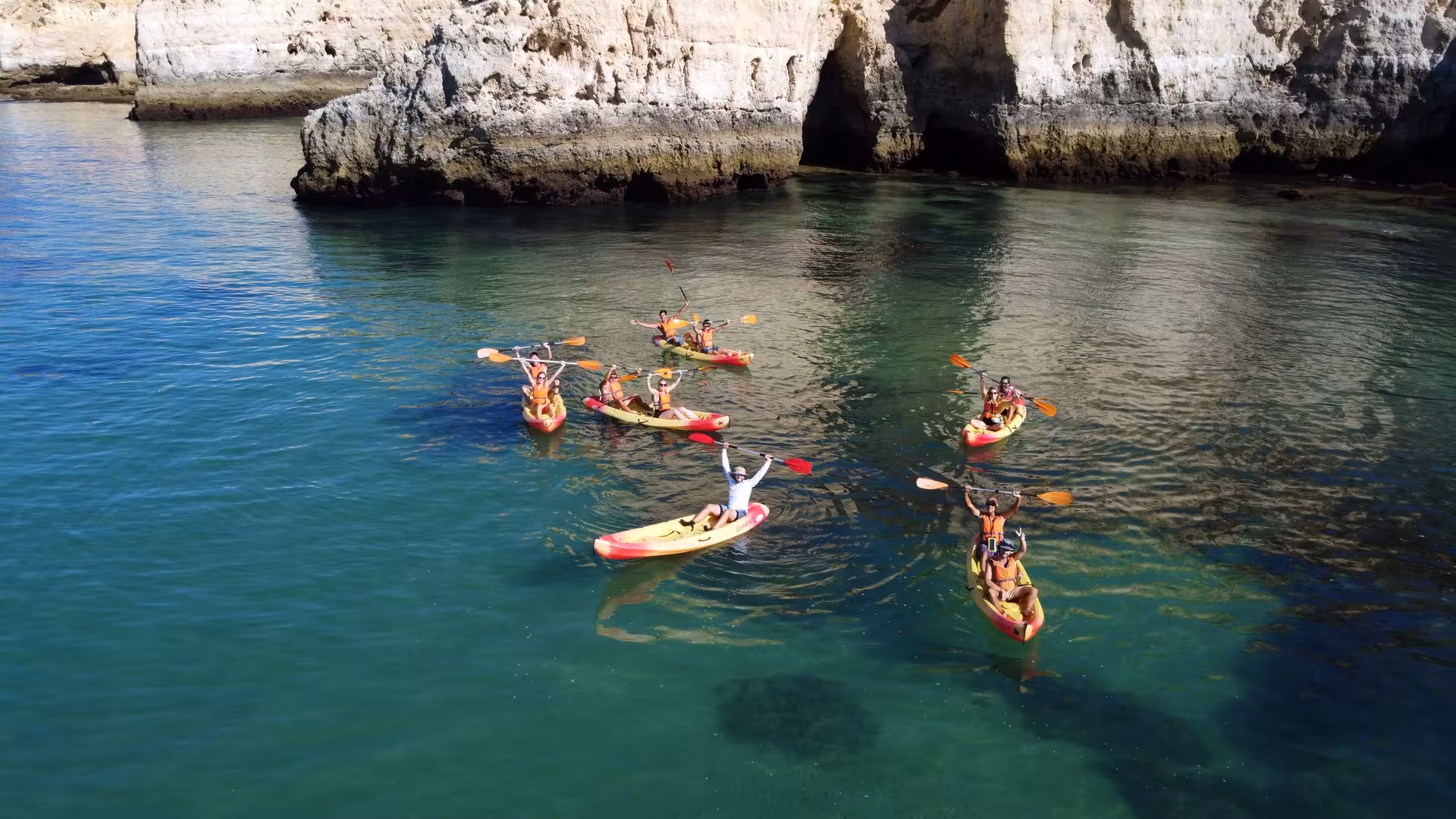 Group of kayakers celebrating on turquoise waters near Algarve sea caves during a Benagil boat tour from Portimao