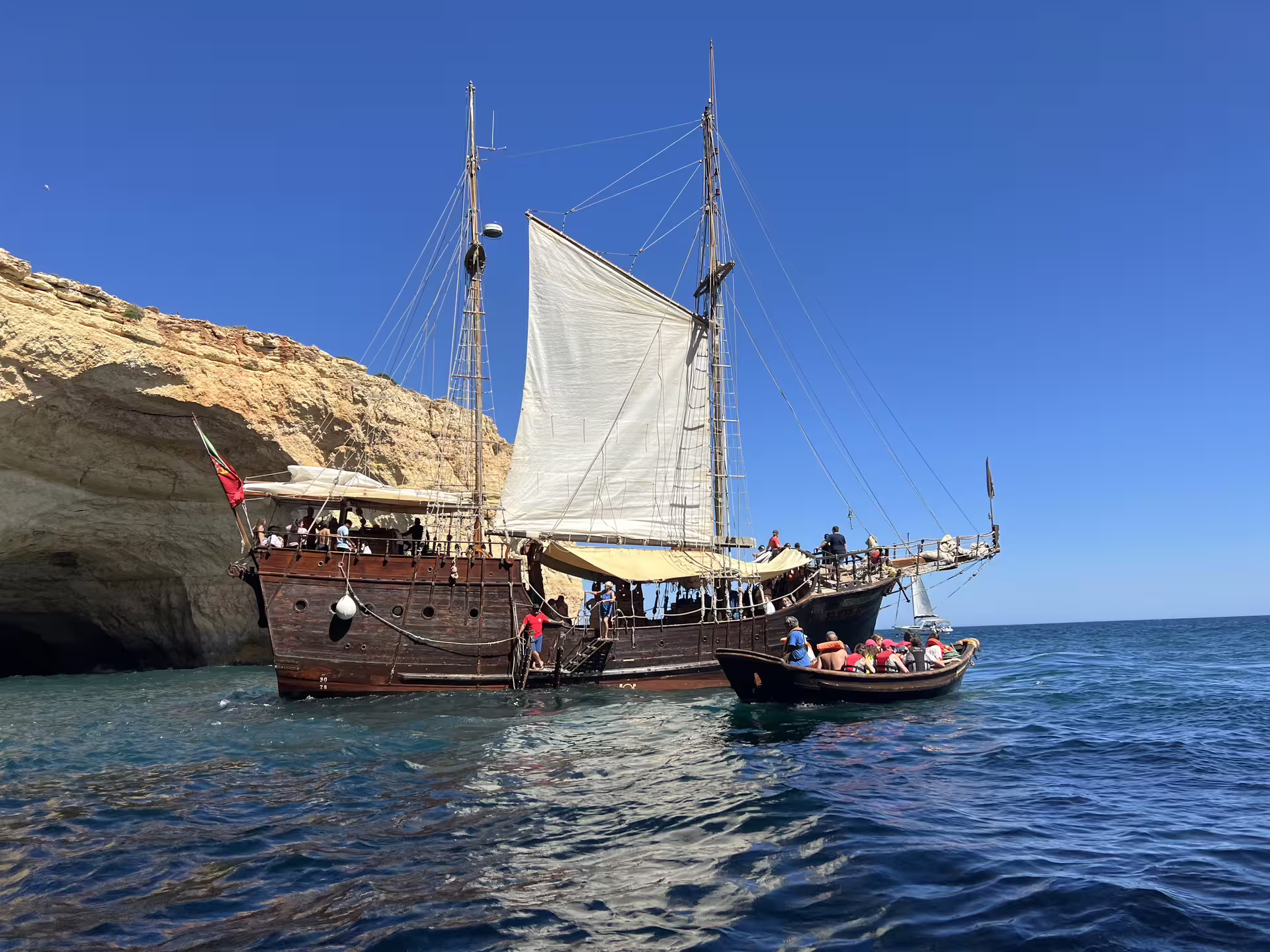 Wooden sailboat anchored near Benagil caves with tourists exploring the scenic Algarve coastline.