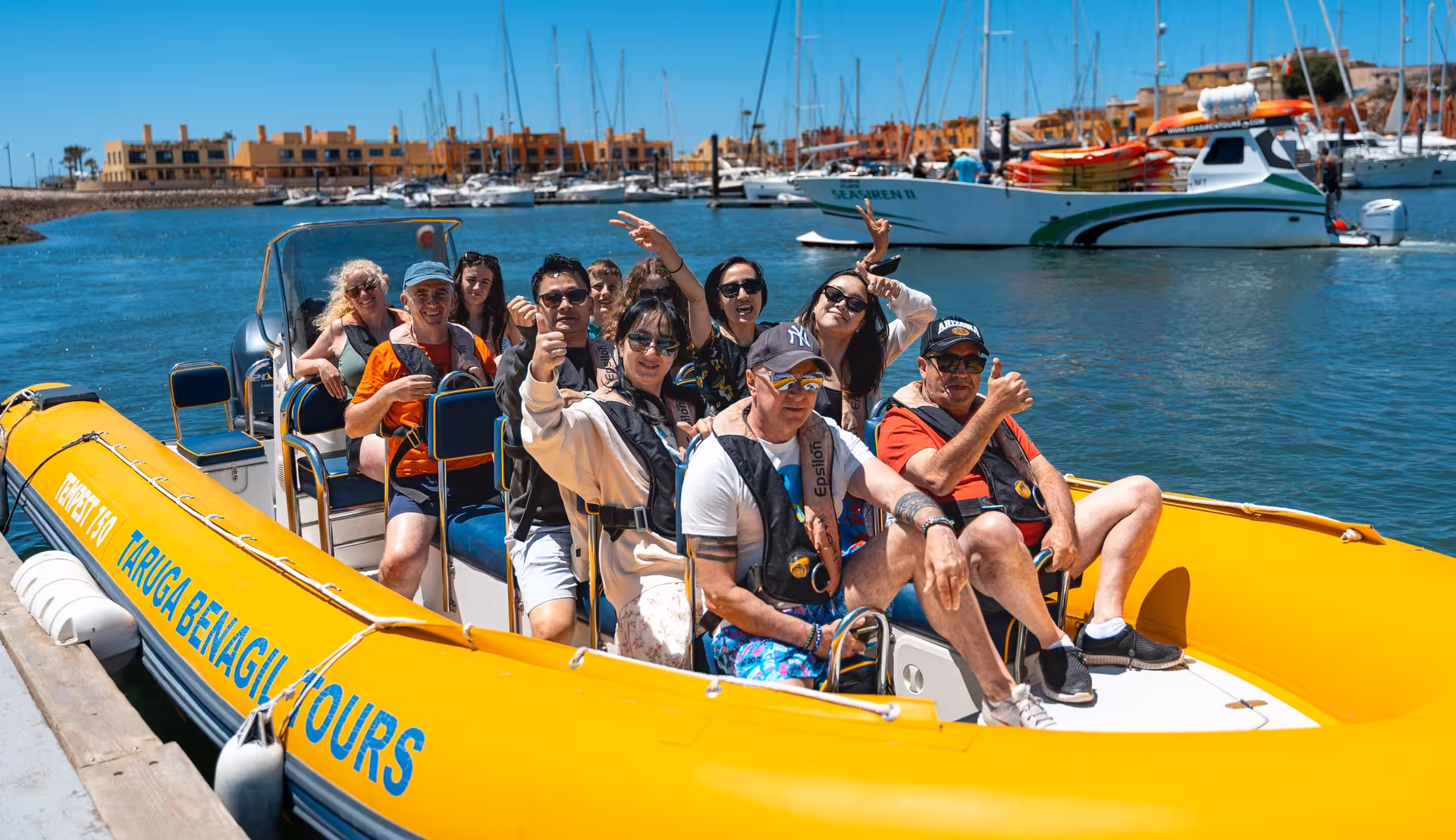 Excited tourists on a yellow Taruga Benagil Tours RIB boat departing Portimao marina for an Algarve coast cave tour
