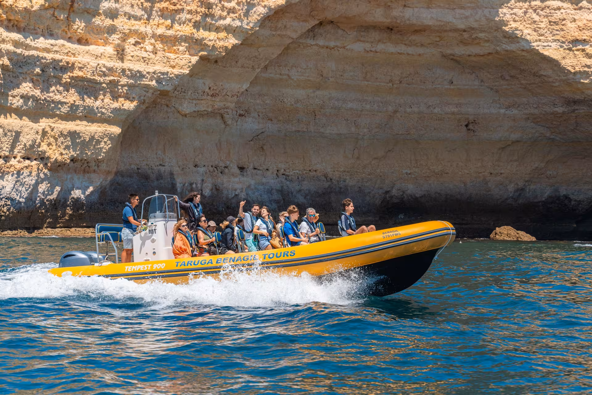 Taruga Benagil Tours speedboat with excited passengers cruising past golden Algarve sea caves from Portimao